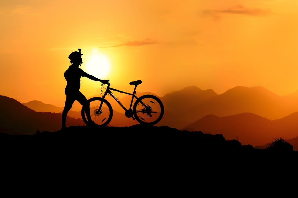 A silhouette of a man standing while holding his bike on top of the mountain