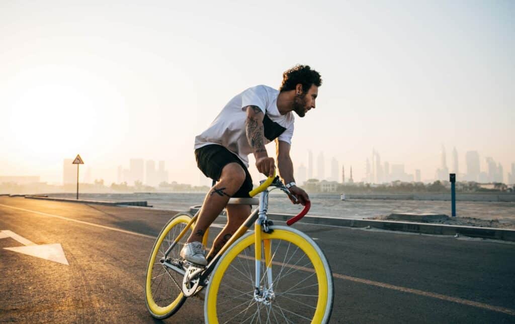 A man riding on a white road bike with white tires and yellow rims