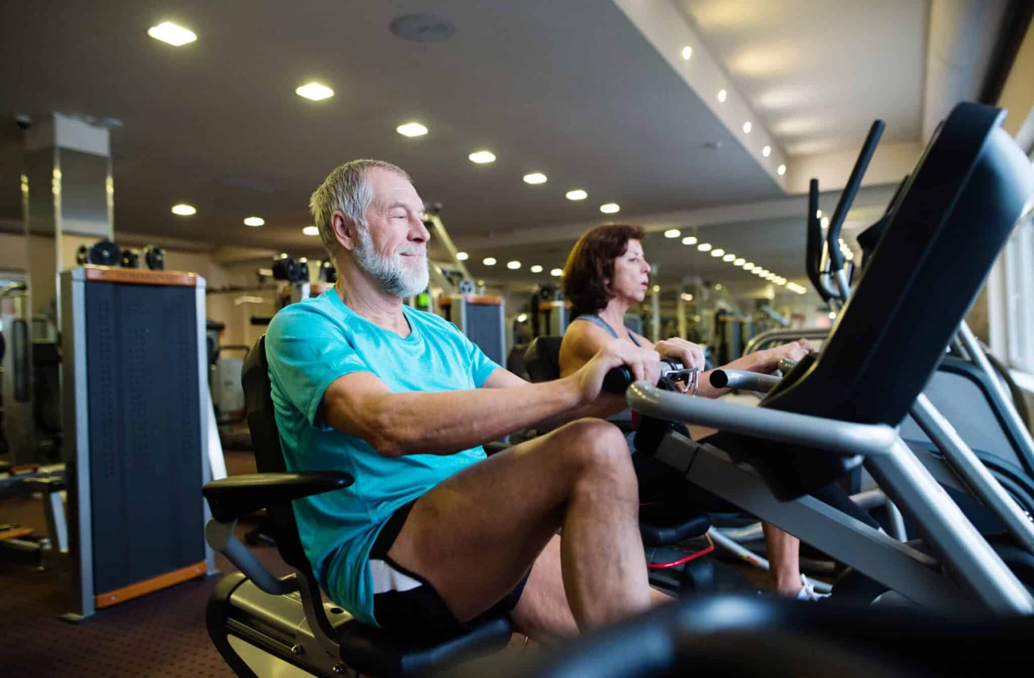 two senior people exercising on recumbent bikes in a gym