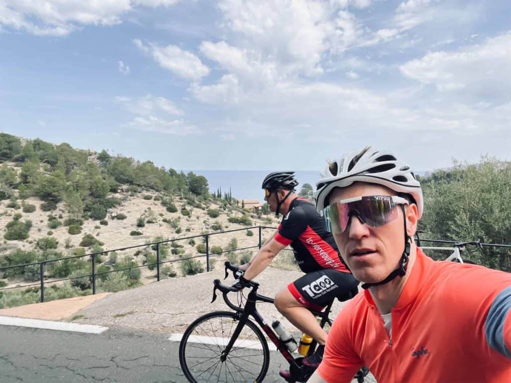 two cyclists riding along a road with sea in background