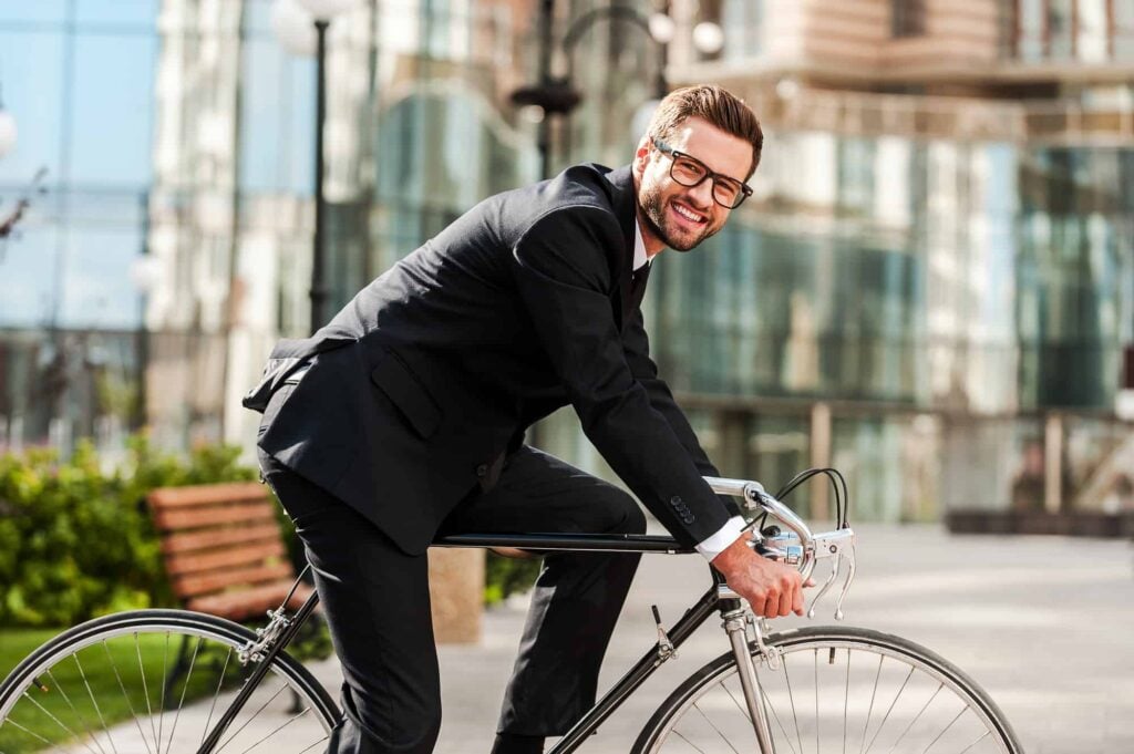 Perfect day for cycling to work. Side view of cheerful young businessman looking at camera and smiling while riding on his bicycle