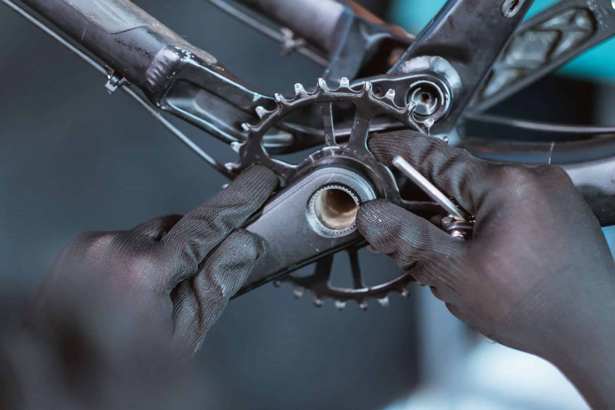 close up of a mechanic’s hand wearing gloves installing the right crank arm on the bottom bracket
