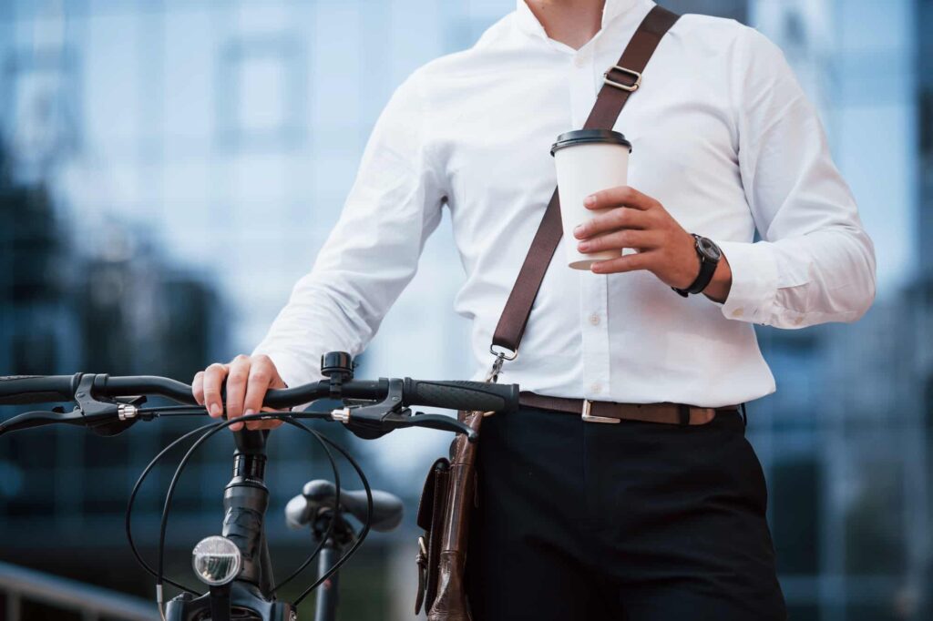 A man is holding a coffee cup while standing next to a bicycle.