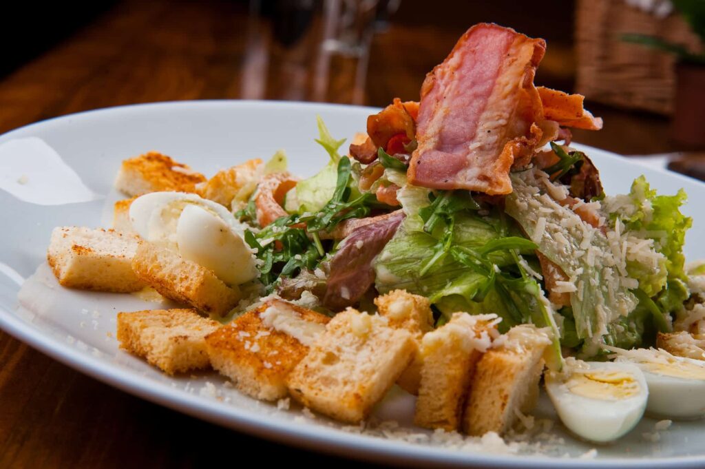 A salad with bacon and croutons on a white plate.