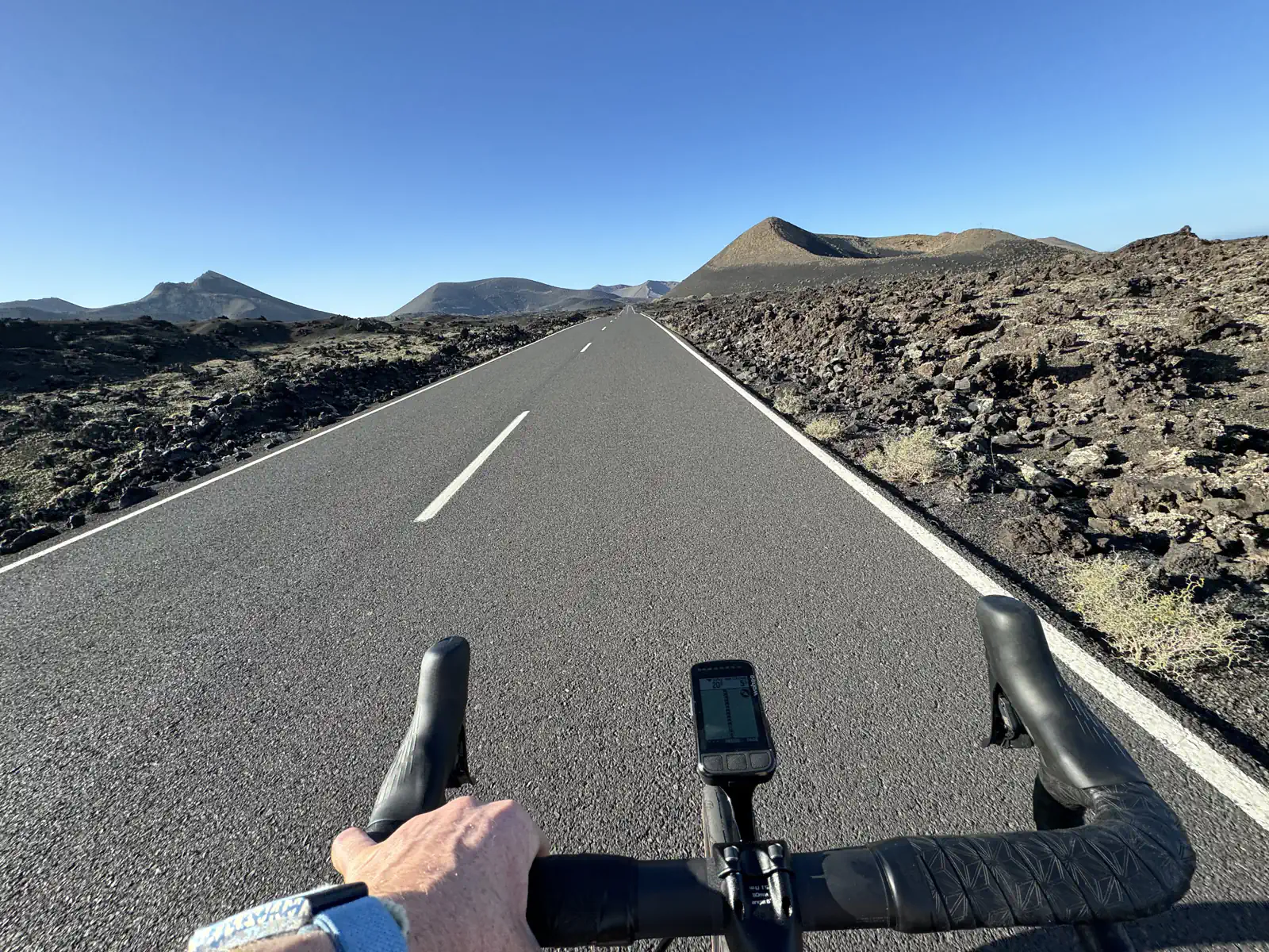 Cyclist's perspective on a road surrounded by volcanic terrain under a clear sky.