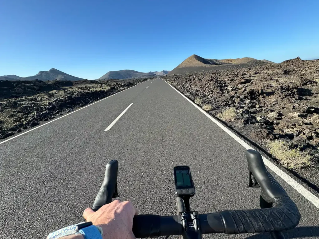 Cyclist's perspective of a road traversing a volcanic landscape with clear skies.