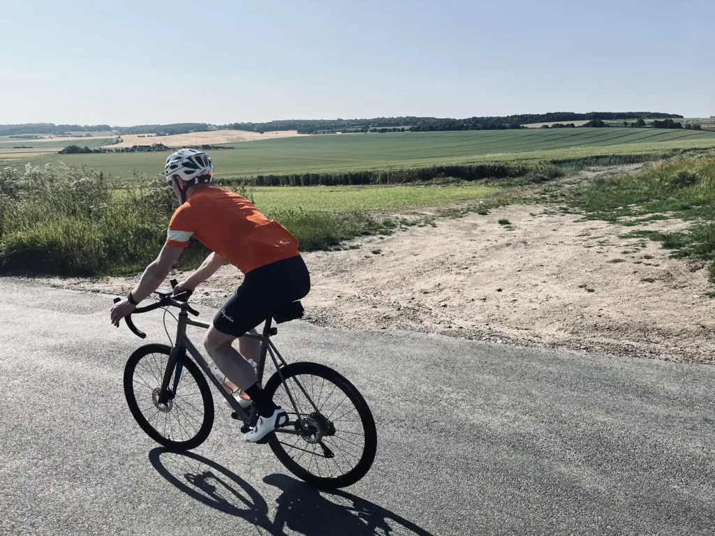 Cyclist riding on a rural road with fields in the background on a sunny day.