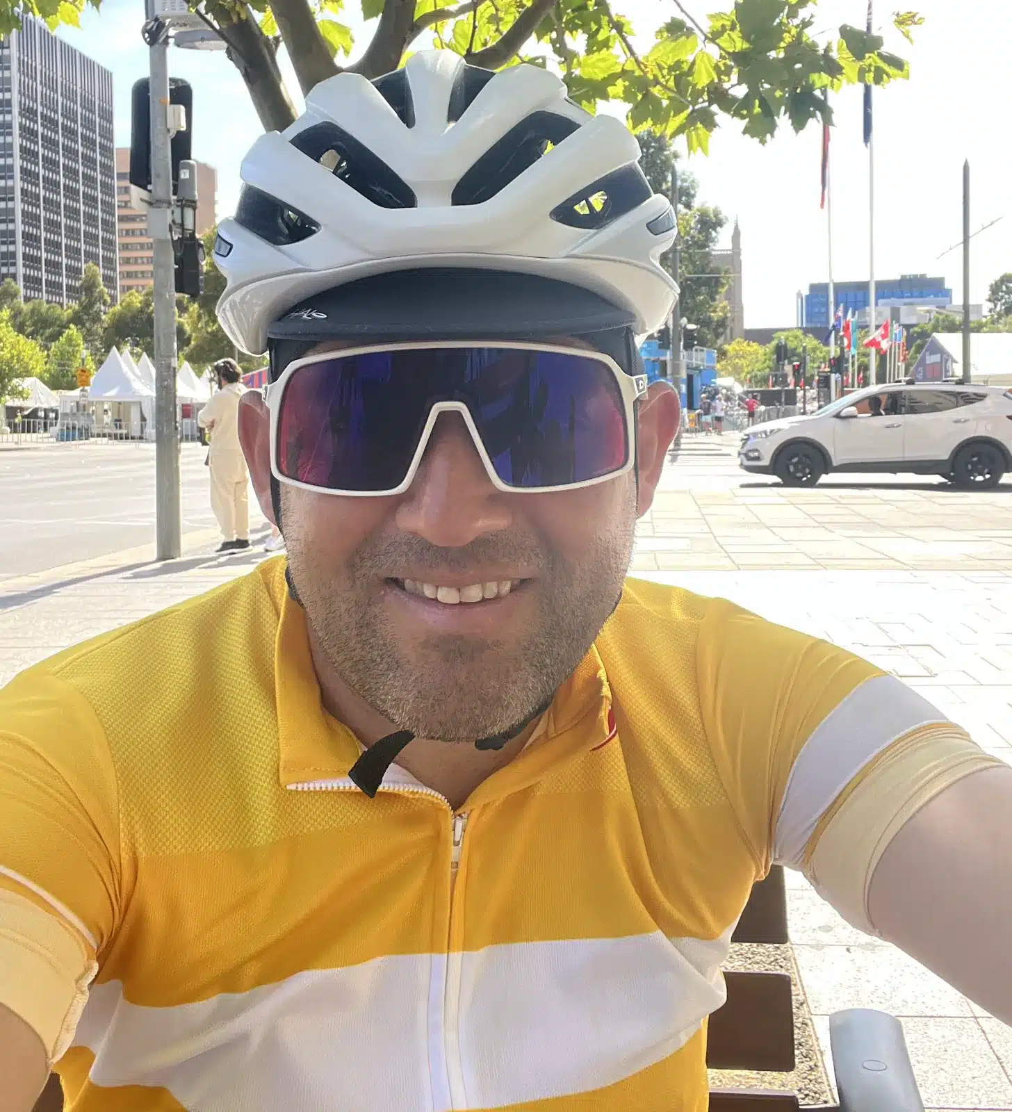 A cyclist wearing a helmet and sunglasses takes a selfie in an urban setting.