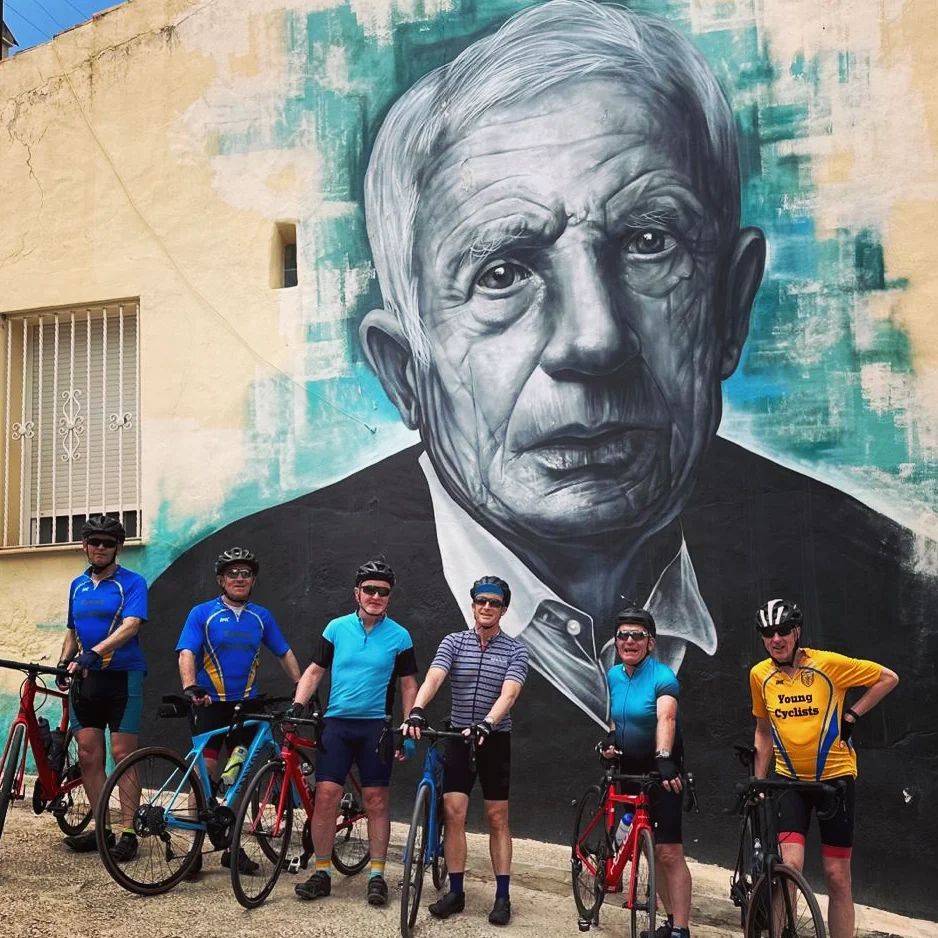 Six cyclists are chilling with their bikes in front of this huge mural of an old guy.