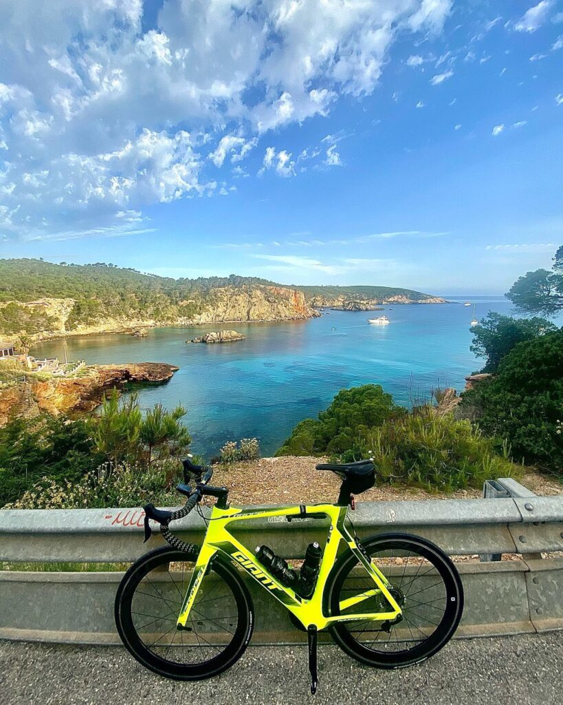 There's this bright green road bike chilling by the roadside with an awesome coastal backdrop—clear blue water, rocky cliffs, and a partly cloudy sky.